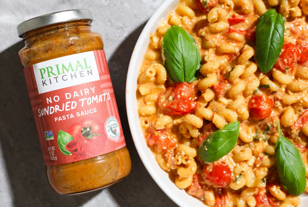 Baked Feta Pasta in a white bowl next to a jar of Primal Kitchen Sundried Tomato Pasta sauce.