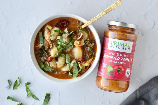 A bowl of Marry Me chicken soup next to a jar of Primal Kitchen Sundried Tomato Pasta sauce.