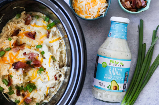 Crockpot ranch chicken in a slow cooker next to a bottle of Primal Kitchen Ranch Dressing. 