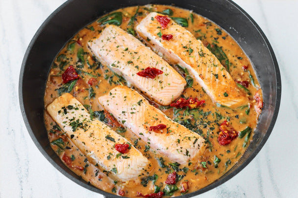 Four salmon filets with sundried tomato sauce in a cast iron skillet.