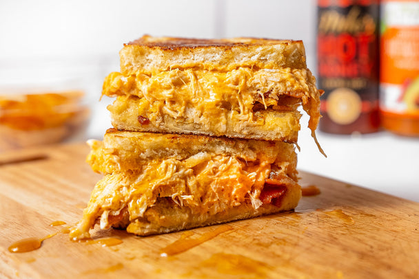 Two halves of a delicious-looking hot honey buffalo chicken sandwich stacked on a wooden cutting board with hot honey drizzled around. 