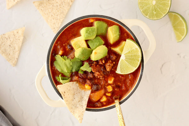 Overhead view of a bowl of taco soup topped with avocado and tortilla chips.