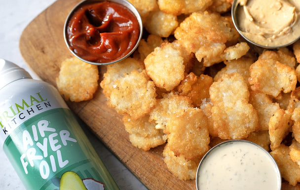 Smashed tater tots on a wooden cutting board with dips, next to a bottle of Primal Kitchen Air Fryer Spray.