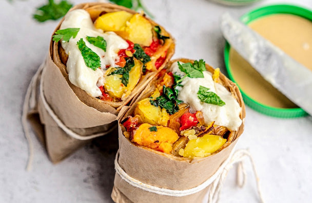 Vegan breakfast burrito cut in half and wrapped in brown parchment paper with white string tied around it. Next to the vegan breakfast burrito is an open jar of Primal Kitchen Vegan Jalapeno Lime Mayo with a knife resting on the lid.