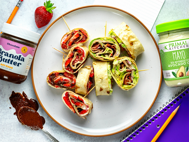 A white plate holds sweet and savory pinwheels with oat butter and mayo, plus school supplies on either side.