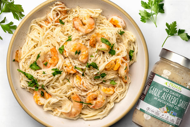 A bowl of Keto Shrimp Alfredo with hearts of palm noodles is next to parsley and a jar of no dairy garlic alfredo sauce.