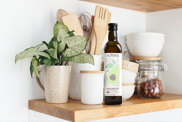 Primal Kitchen Avocado Oil on a shelf with plants and cooking utensils