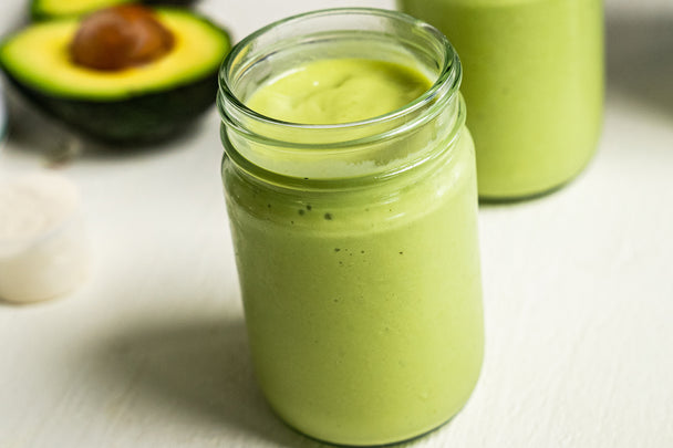 A mason jar is filled with a keto avocado smoothie, with collagen fuel and avocados near by.