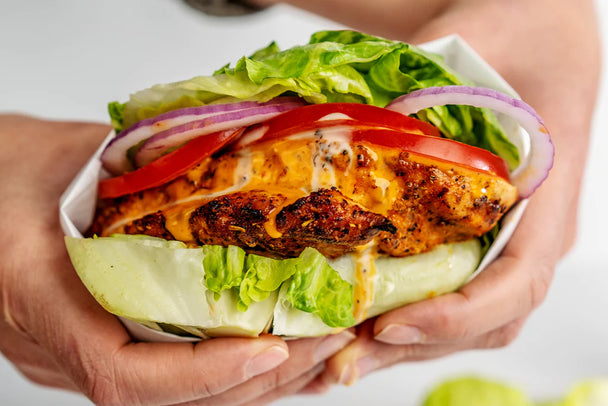 a grilled buffalo chicken sandwich lays next to ingredients and a bottle of buffalo sauce.