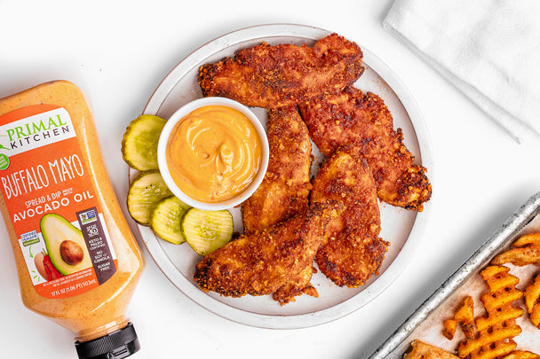 A plate of air fryer chicken tenders with a side of mayo, next to a bottle of Primal Kitchen Squeeze Buffalo Mayo