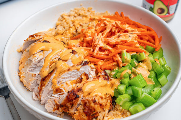 A bowl of cut chicken, shredded carrots, chopped celery and cauliflower rice with Primal Kitchen Buffalo Ranch Dressing