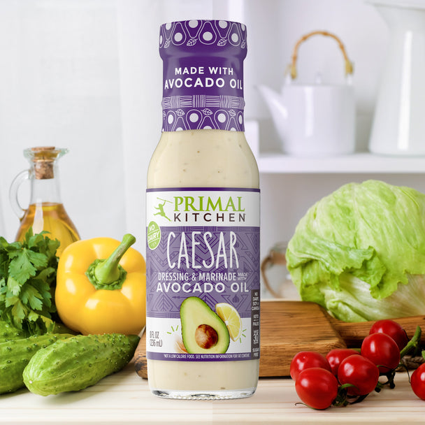 A bottle of Primal Kitcheb Caesar Dressing on a countertop with vegetables.