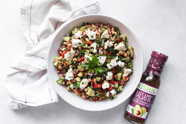 Overhead view of a bowl of black eyed pea salad next to a bottle of Primal Kitchen Balsamic Dressing and a napkin.