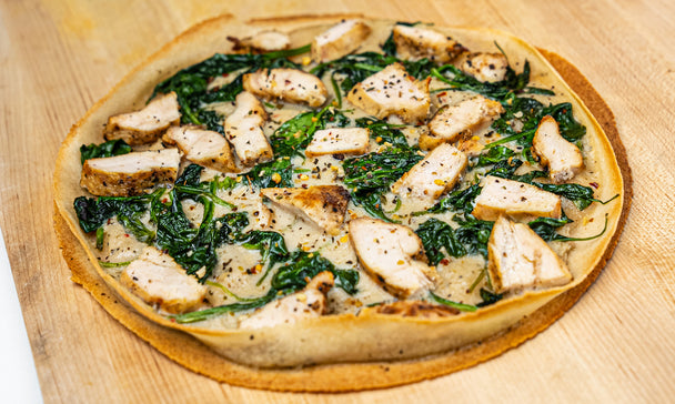 White pizza sauce lays next to white pizza with spinach on a cutting board.