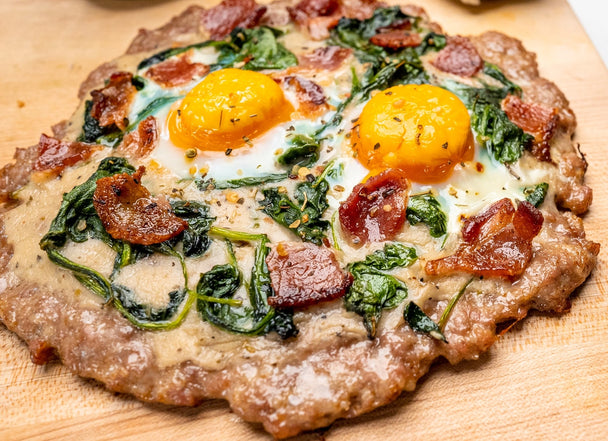 A breakfast meatza pizza sits on a cutting board.