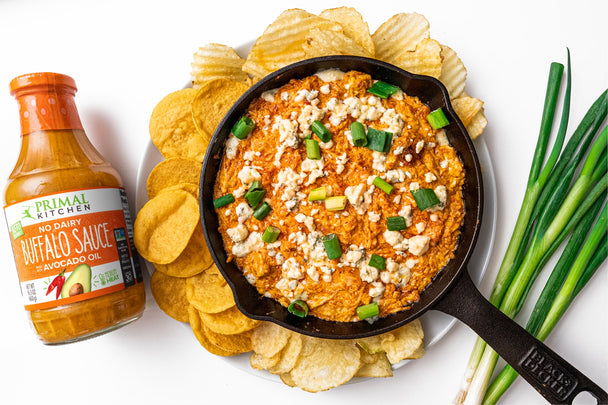 A bottle of Costco-sized buffalo sauce is next to keto buffalo chicken dip surrounded by chips and green onions.