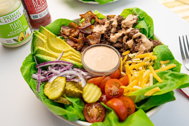 Deconstructed bison burger in a bowl with Primal Kitchen Mayo & Ketchup in the background