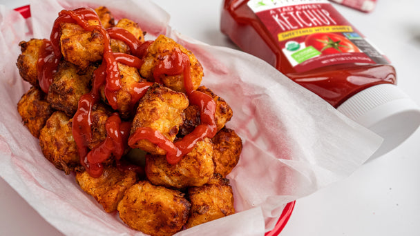 basket of homemade tater tots with ketchup squeezed on top and a bottle of Primal Kitchen A Tad Sweet Squeeze Ketchup in the background.