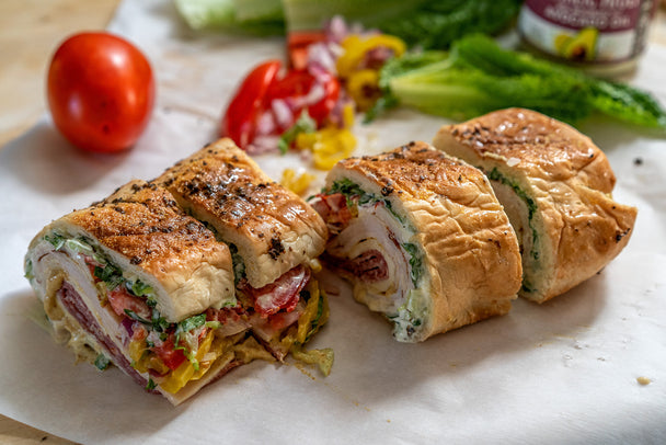 A garlic aioli sandwich cut into four pieces on white parchment paper, with vegetables in the background.