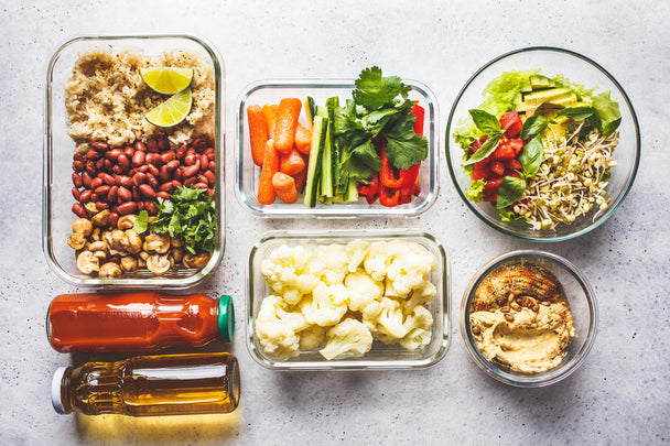 Overhead view of colorful, plant-based meals and snacks in glass storage containers.