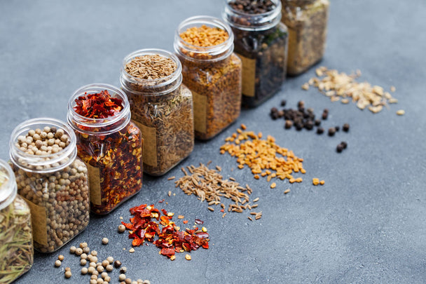 A row of glass spice jars with some spices spilled on the counter. 