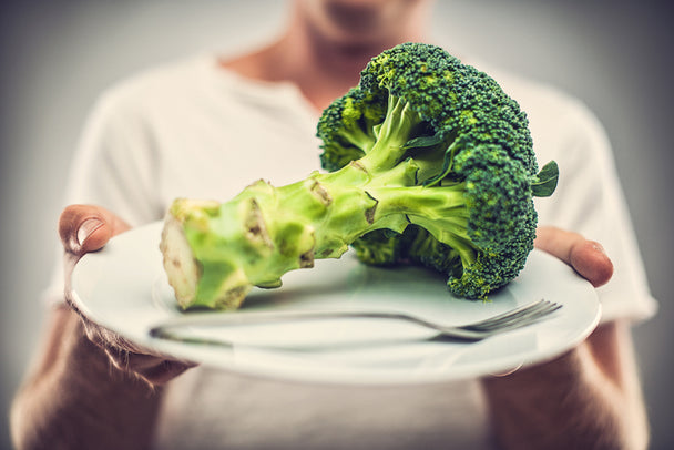 closeup on a broccoli stalk on a white plate, with a person holding the plate