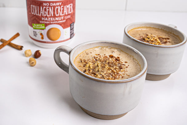 Hazelnut collagen creamer stands behind two cups of hazelnut collagen lattes topped with chopped nuts.