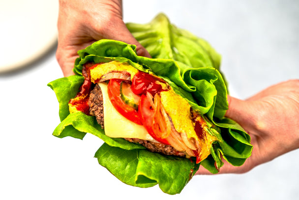 Two hands holding a delicious classic cheeseburger wrapped in lettuce.