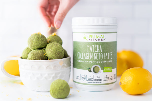 A hand sprinkling lemon zest on top of matcha balls stacked in a white bowl. Next to the bowl is a canister of Primal Kitchen Matcha Collagen Keto Latte Drink Mix and lemons.