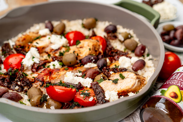 Mediterranean chicken with cauliflower rice in a cast iron skillet, next to a bottle of Primal Kitchen Balsamic Vinaigrette and Marinade.  