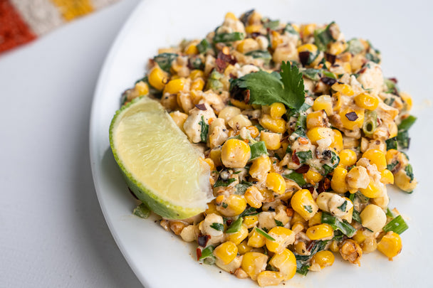 Closeup on Mexican Corn Salad made with Primal Kitchen Mayo on a white plate, garnished with a lime wedge. 