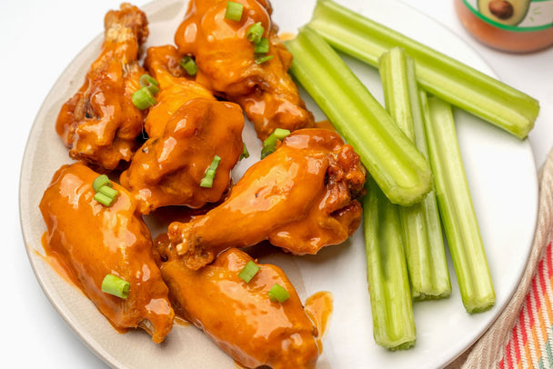 Crispy, mild Buffalo chicken wings with celery sticks on a white plate.