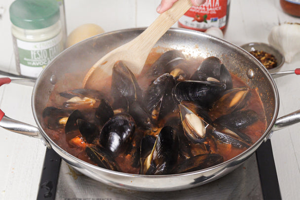 Mussels Fra Diavolo is stirred by a wooden spoon with Pesto Mayo and Arrabbiata behind it.