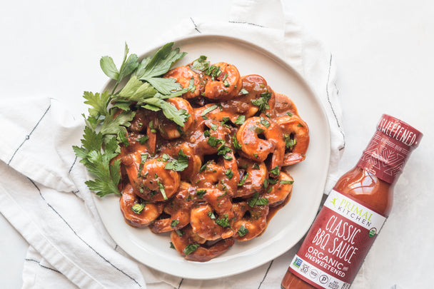 A plate of BBQ Shrimp with a side of parsley, next to a bottle of Primal Kitchen BBQ Sauce