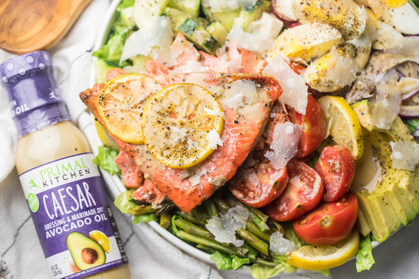 A close up of a salmon caesar salad next to a bottle of Primal Kitchen Caesar Dressing