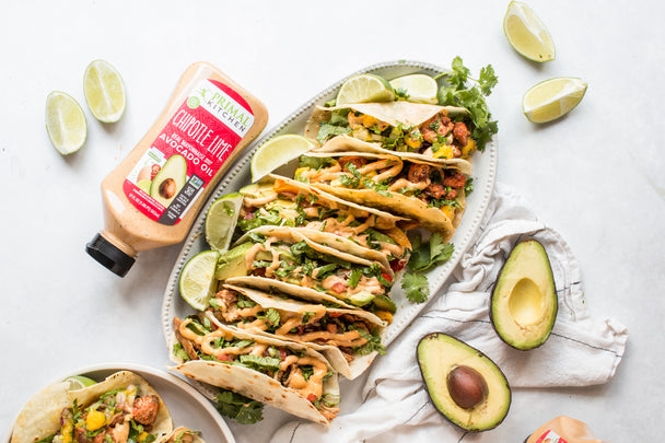 A plate of tacos on a white table next to a bottle of Squeeze Chipotle Lime Mayo