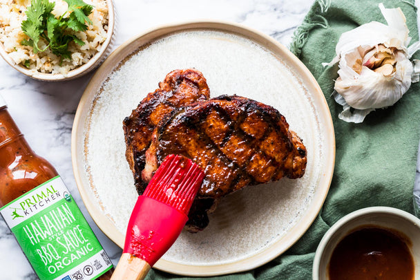 Grilled BBQ pork chops being brushed with Primal Kitchen Hawaiian-Style BBQ Sauce