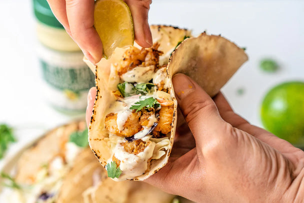 Hands holding pesto shrimp tacos made with Primal Kitchen Pesto Mayo. 