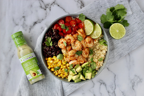 A delicious bowl of shrimp and vegetables next to a bottle of Primal Kitchen Cilantro Lime Dressing. 