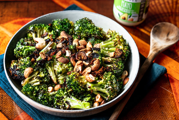 A white bowl of fig and sage roasted broccoli salad on a colorful background with a wooden spoon on the right side.