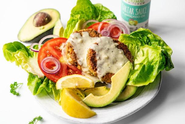 Keto Salmon Burgers with Primal Kitchen Tartar Sauce on a bed of bibb lettuce with sliced red onion, tomatoes, avocado, and lemon