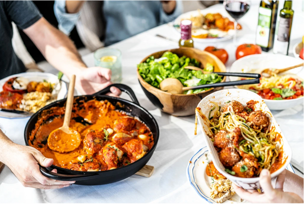 A table of real food favorites is being shared with two hands holding dishes.