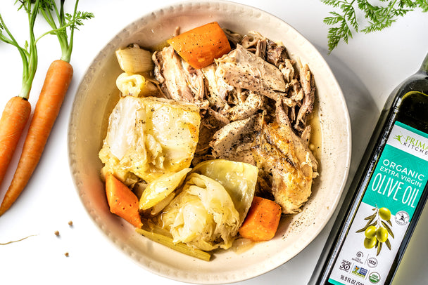 Slow roasted chicken with roasted cabbage and carrots in a big white bowl. A bottle of Primal Kitchen Extra Virgin Olive Oil and carrots are next to the white bowl.