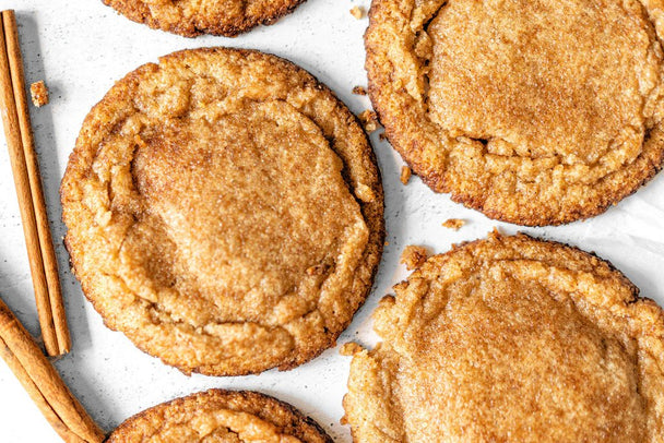 Snickerdoodle cookies next to Primal Kitchen Snickerdoodle Collagen Fuel with cinnamon sticks