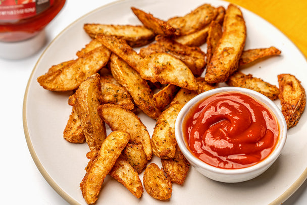 Air Fryer Potato Wedges on white paper next to Primal Kitchen Ketchup