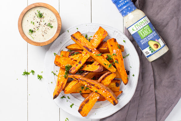 A white plate with vegan sweet potato fries, next to a bottle of Primal Kitchen Plant Based Ranch.