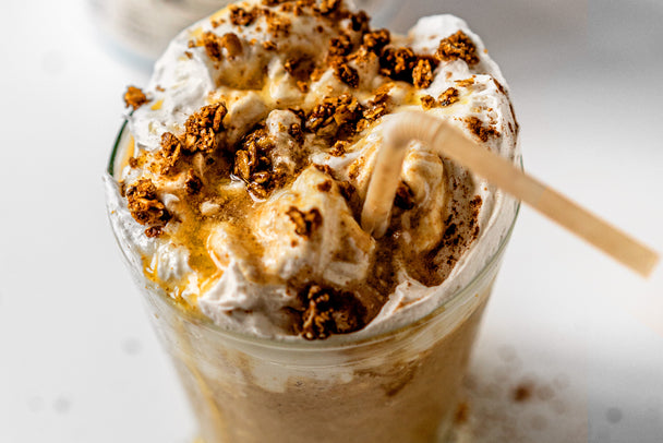 An apple pie smoothie with collagen is topped with granola and served in a clear cup with a straw.