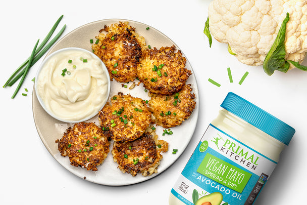 Cauliflower fritters are on a white plate with ingredients like vegan mayo and caulflower nearby.