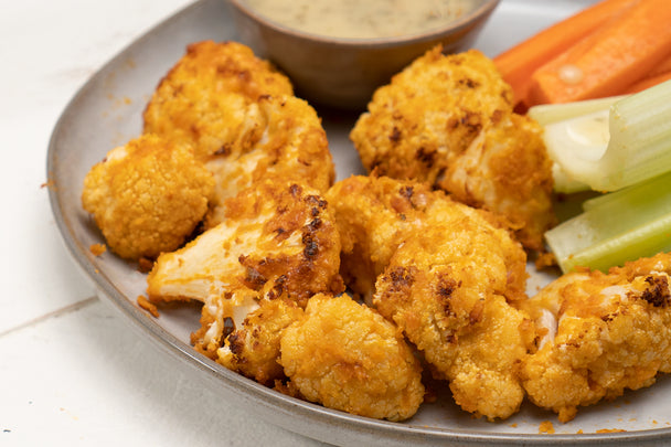 Closeup of air-fried cauliflower wings on a plate with celery and carrot sticks. 