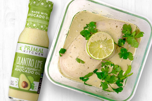 Chicken marinating in a square baking dish next to a bottle of Primal Kitchen Cilantro Lime Dressing.